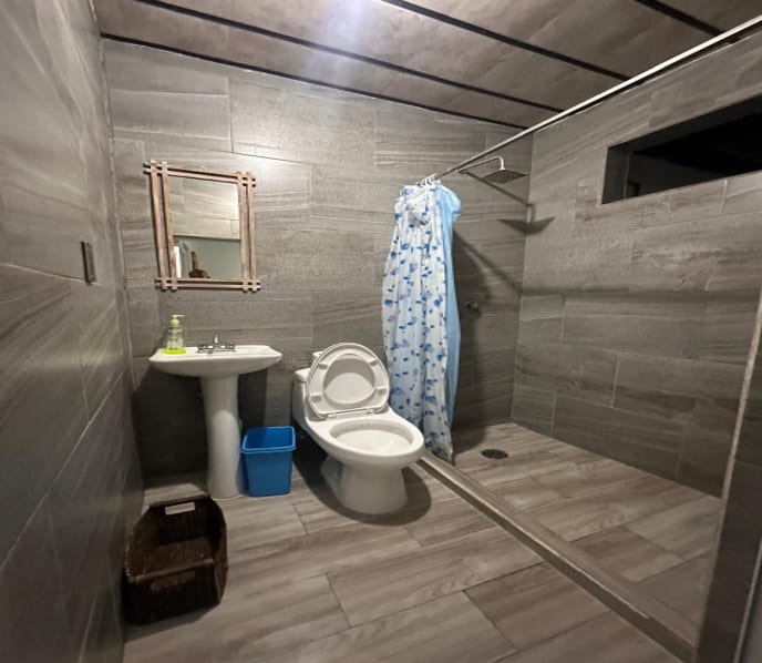 Baño con regadera, lavabo y acabados en loseta gris