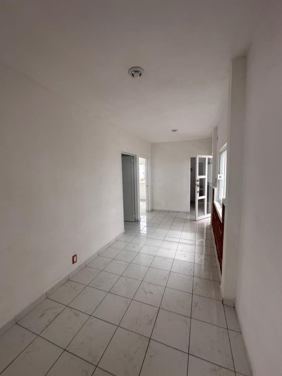 Vista de la estancia hacia las dos recámaras, con acabados blancos y piso de loseta clara